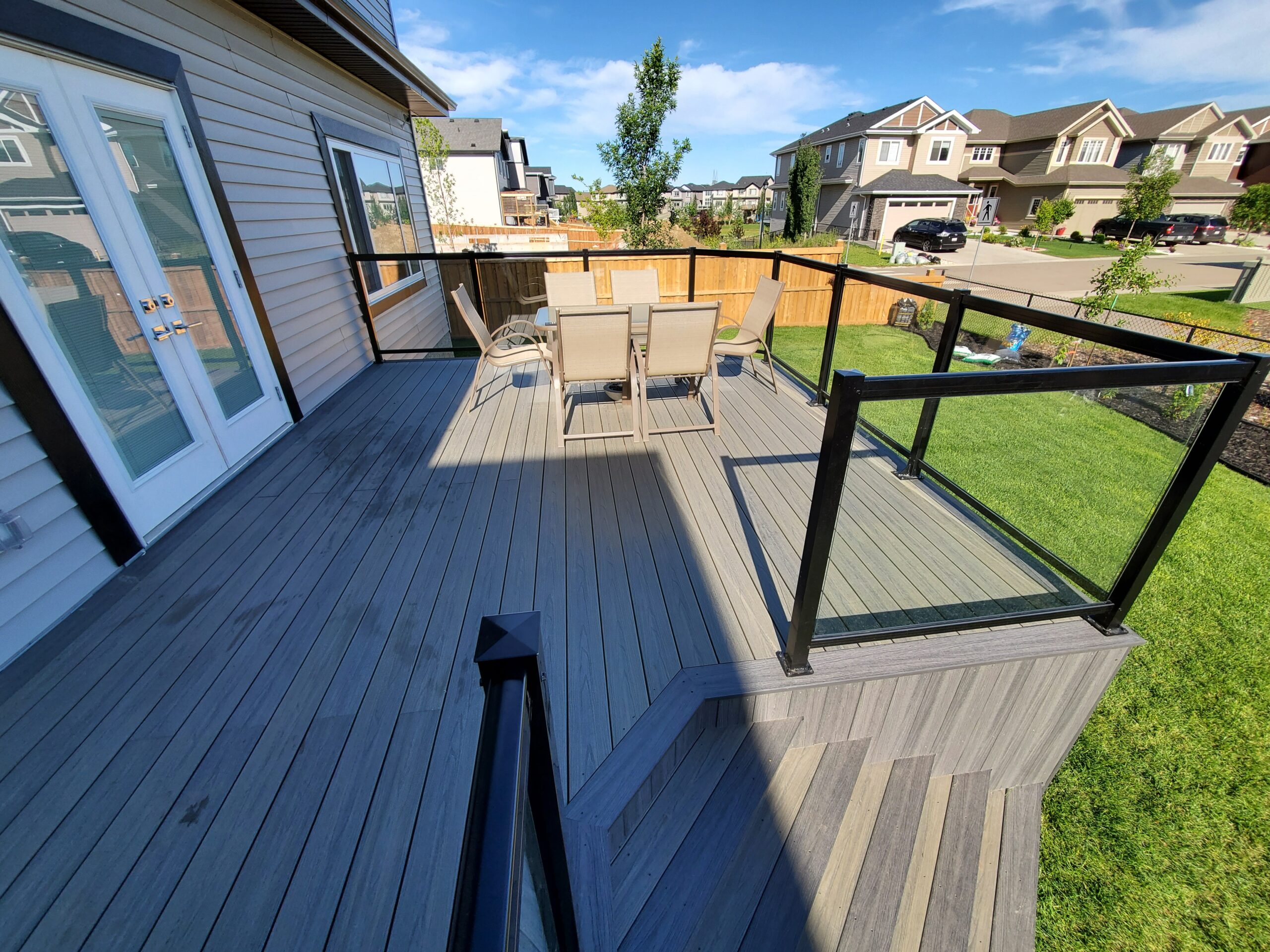 Composite deck with black aluminum and glass railing, wide stairs, and backyard view in Edmonton, Alberta