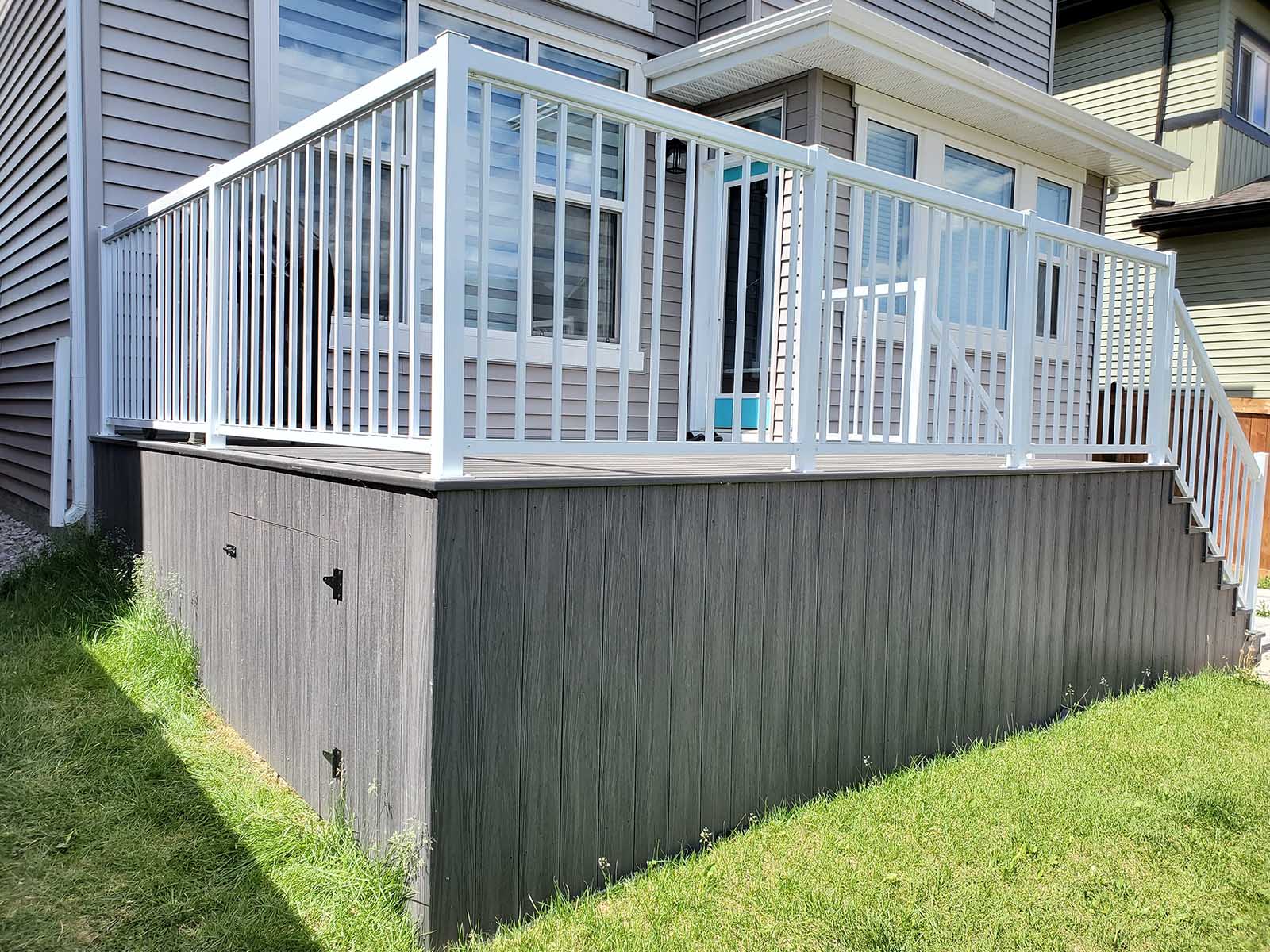 Grey composite deck with composite skirting, built-in storage access, and white aluminum railing built by Crestfield Decking in Edmonton, Alberta