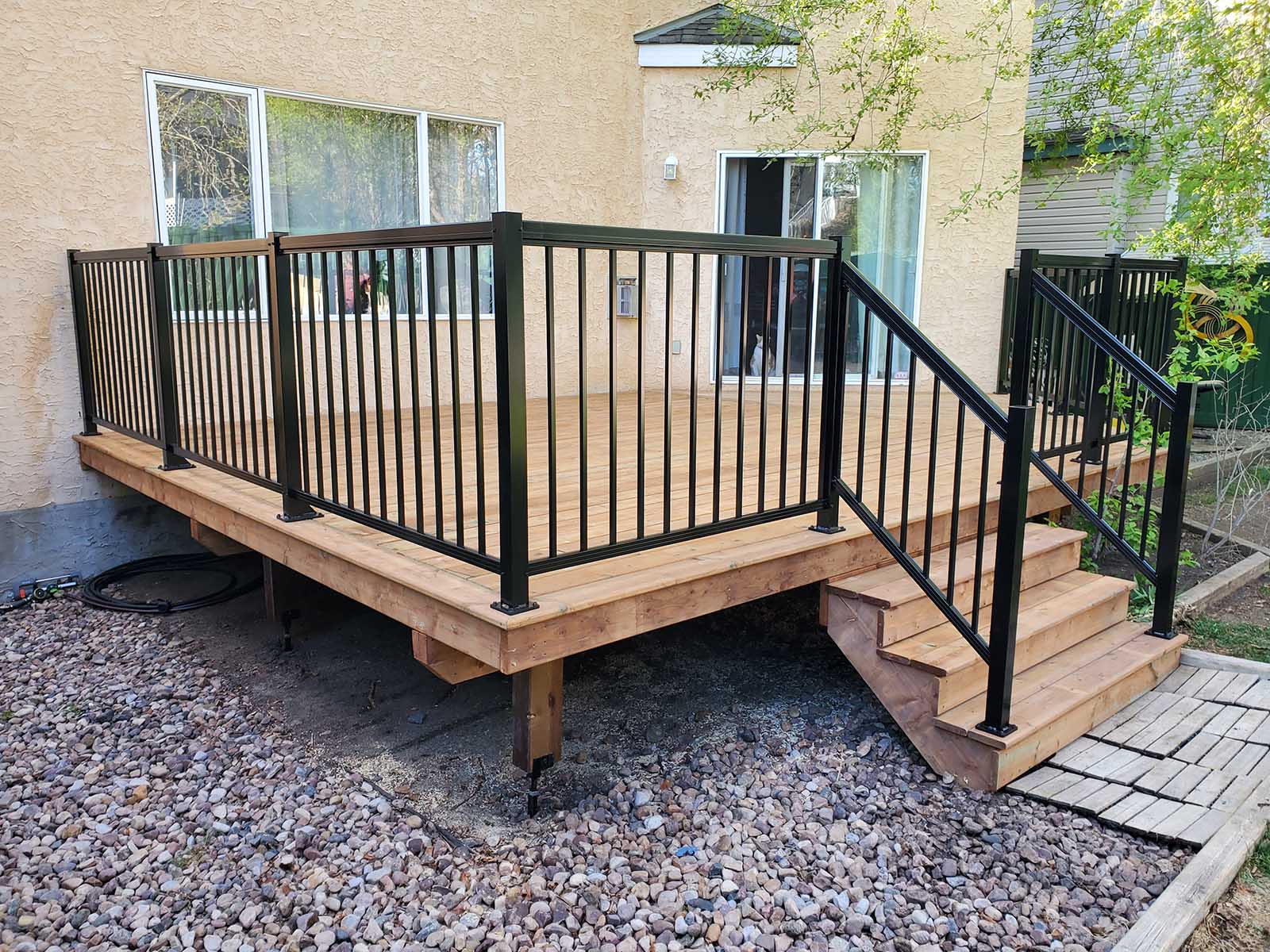 Corner view of pressure-treated deck with black aluminum picket railing and stairs built by Crestfield Decking in Edmonton, Alberta