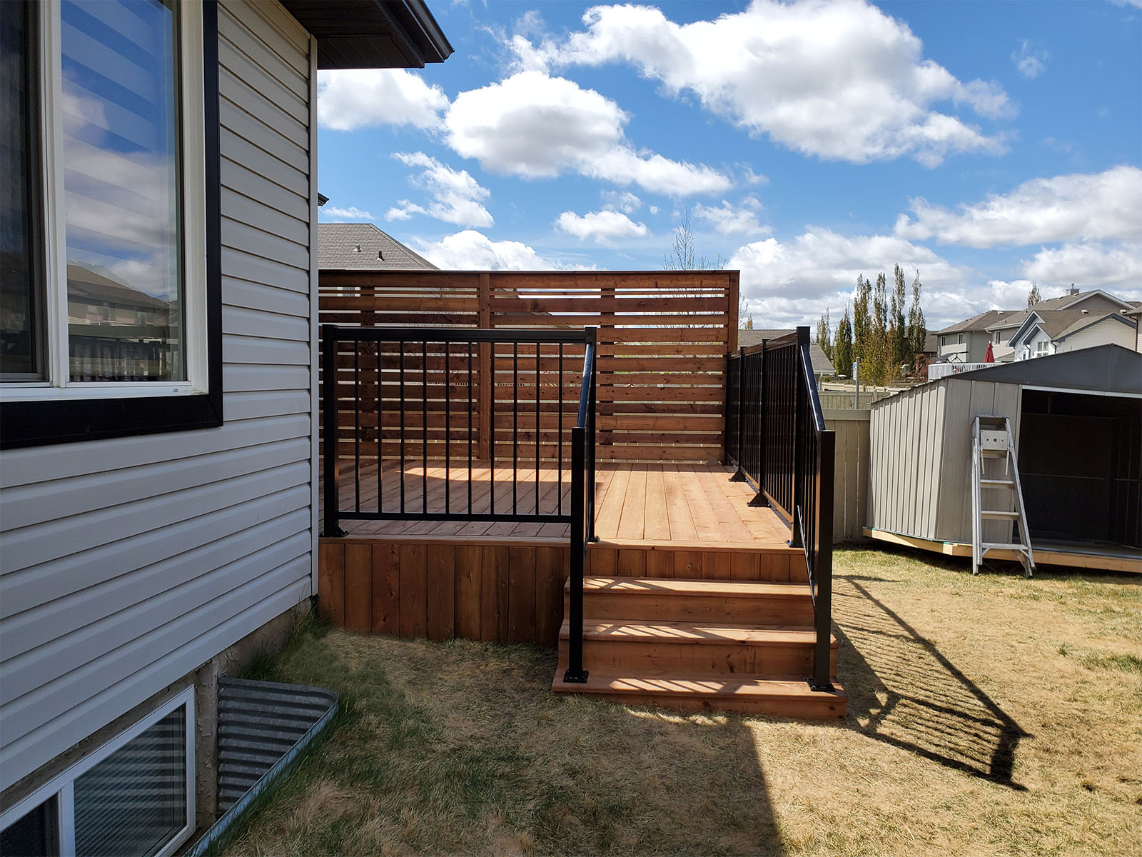 Side view of pressure-treated deck with horizontal privacy screen and black aluminum railing built by Crestfield Decking in Edmonton, Alberta