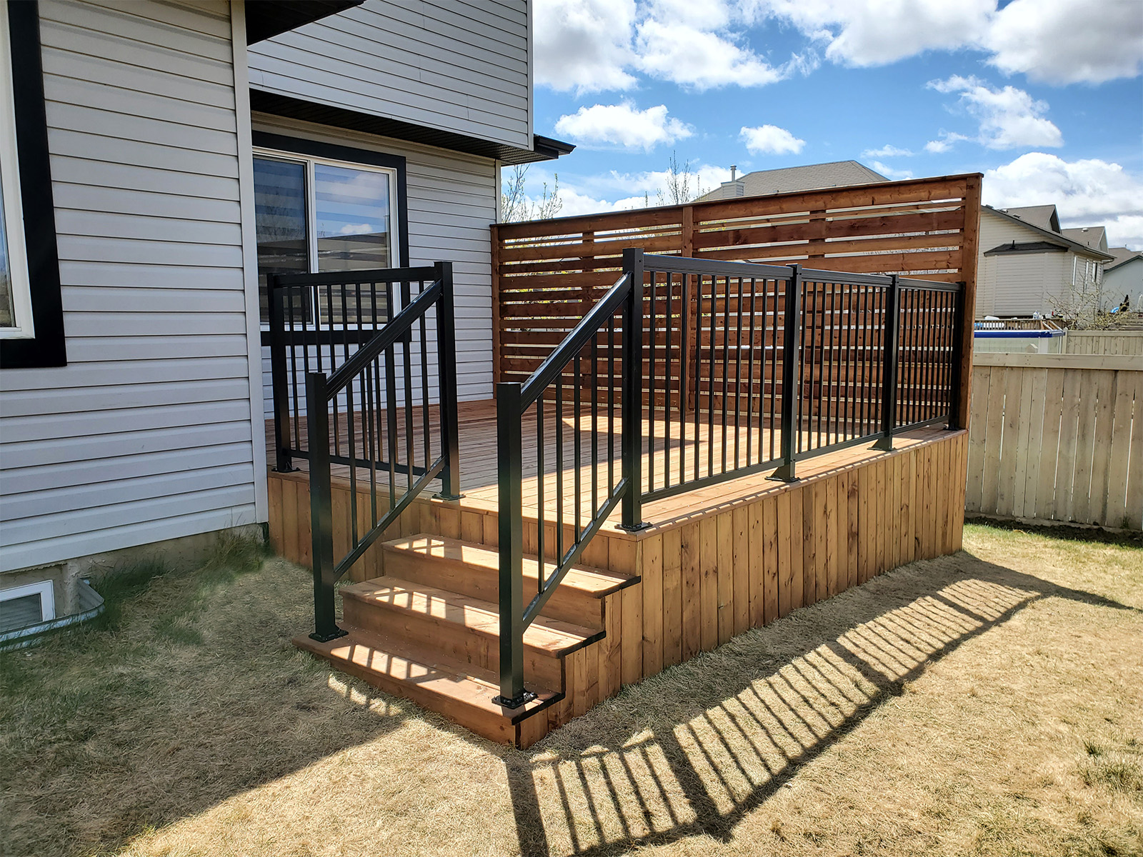 Pressure-treated deck with horizontal privacy screen, stairs, and black aluminum railing built by Crestfield Decking in Edmonton, Alberta