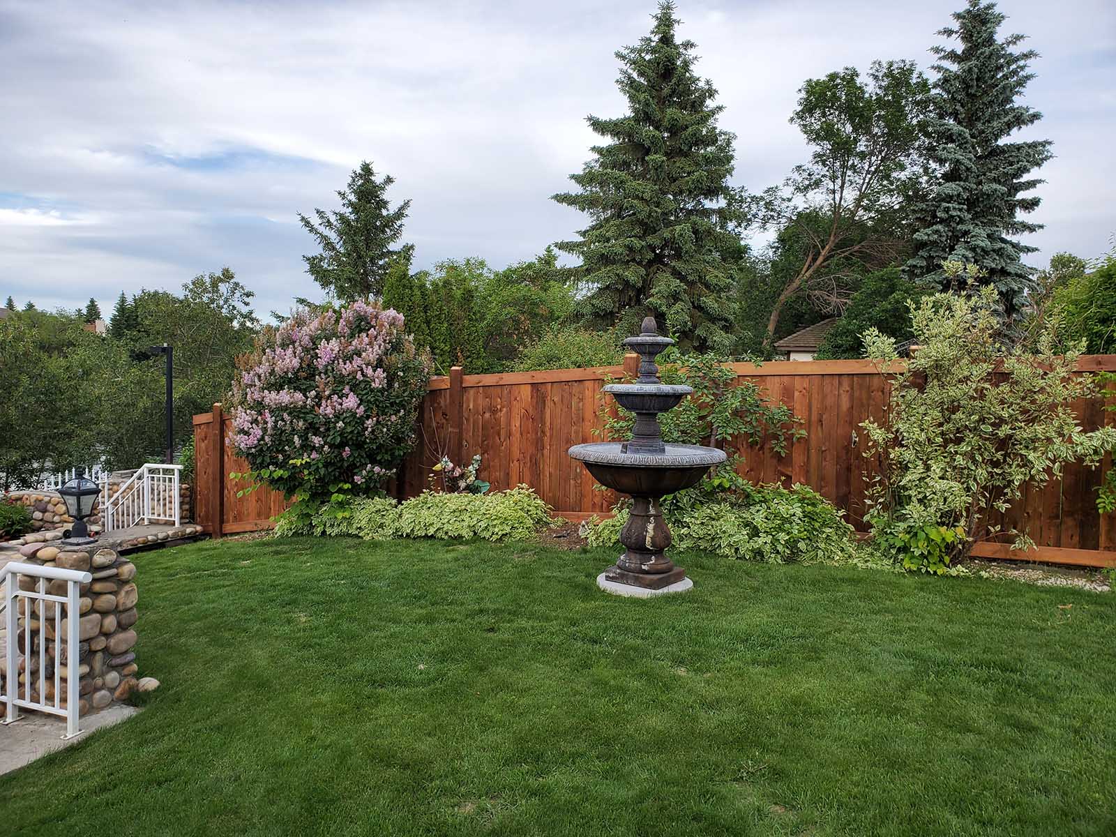 Pressure-treated privacy fence surrounding a landscaped backyard with fountain built by Crestfield Decking in Edmonton, Alberta